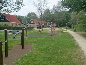 Een speeltuin met schommels, glijbanen en klimtoestellen, omringd door gras en bomen.