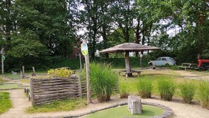Un parcours de minigolf avec un pont en bois, une table de pique-nique et une voiture garée à proximité.