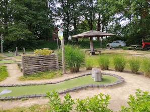 Un parcours de minigolf avec un pont en bois, une table de pique-nique et une voiture garée à proximité.