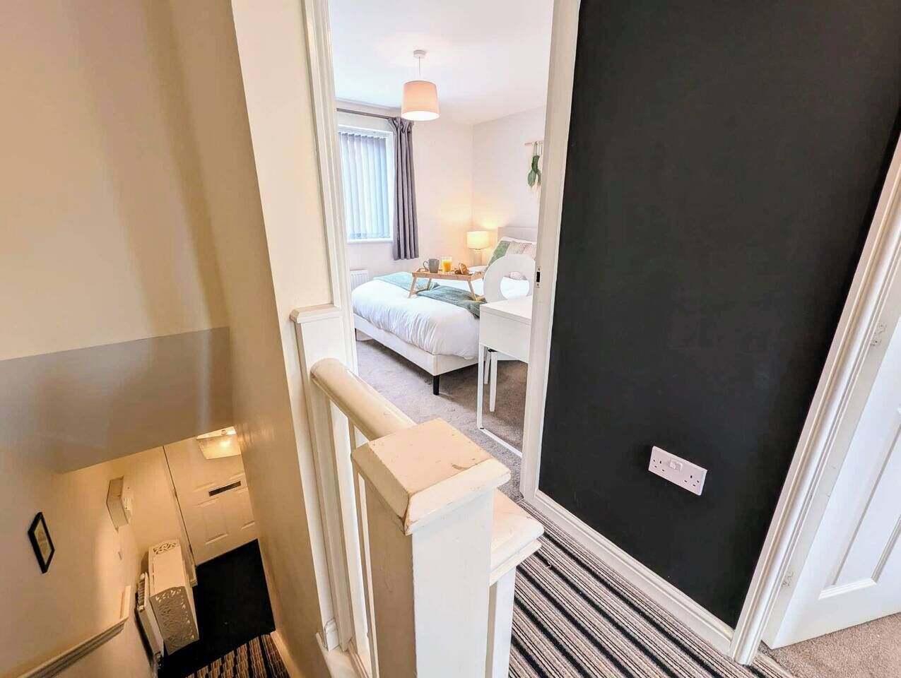 A hotel room with a bed, bedside table, lamp, and a view of the hallway.