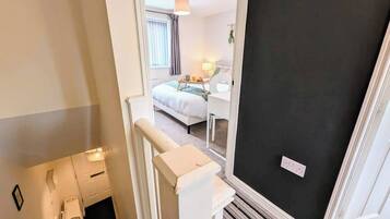 A hotel room with a bed, bedside table, lamp, and a view of the hallway.