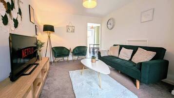 A living room with a TV, green chairs, a white coffee table, and a green sofa.