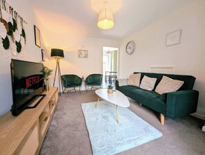 Ein Wohnzimmer mit Fernseher, grünen Sesseln, einem weißen Couchtisch und einem grünen Sofa.