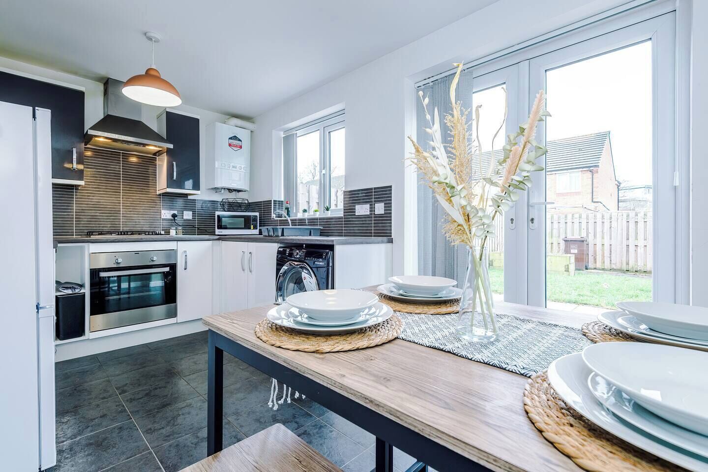 A modern kitchen with a dining area, large windows, and a view of the backyard.