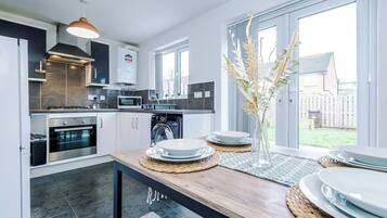 A modern kitchen with a dining area, large windows, and a view of the backyard.