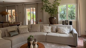 Ein Wohnzimmer mit einer Eckcouch, einer großen Topfpflanze und einem Essbereich mit Tisch und Stühlen.