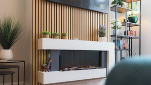 A modern living room with a fireplace, wooden slats, a bookshelf, and a potted plant. - Heath Lodge - Ideal for Families, Contractors & Professionals. (Warwickshire)