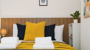 A neatly made bed with a striped headboard, a bedside lamp, and a potted plant on the right.