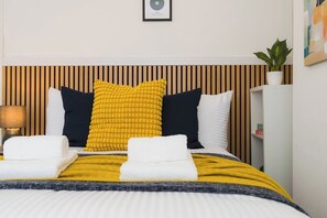 A neatly made bed with a striped headboard, a bedside lamp, and a potted plant on the right. - Heath Lodge - Stockingford, Nuneaton (Warwickshire)