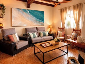 Ein Wohnzimmer mit einer Couch, Sesseln, einem Couchtisch und einem Gemälde einer Strandansicht.