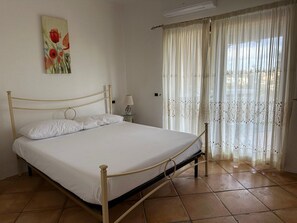 A bedroom with a bed, curtains, a painting, and a lamp. - Charming apartment in Porto Cervo, Sardegna. (Porto Cervo)