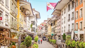 Una calle flanqueada por edificios de varios pisos, algunos con balcones, y una bandera ondeando.