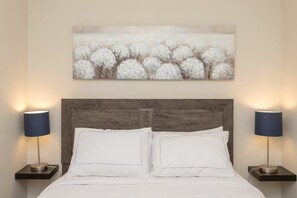 Ein Bett mit weißer Bettwäsche, zwei Nachttischlampen und ein Wandbild mit weißen Blumen.