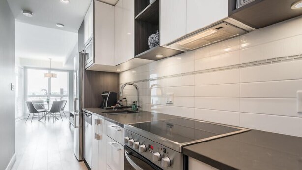 Una cocina moderna con electrodomésticos de acero inoxidable, salpicadero de azulejos blancos y un comedor con mesa y sillas.