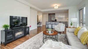 Een moderne woonkamer met een flatscreen televisie, een bank, een salontafel en een eethoek met stoelen.