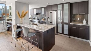 A modern kitchen with dark cabinetry, stainless steel appliances, a marble island, and bar stools.