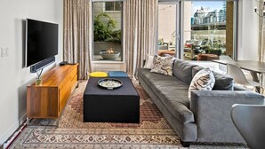 A modern living room with a flat-screen TV, a sofa, a coffee table, and a view of the city through large windows.