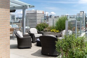 A rooftop terrace with wicker furniture, a glass railing, and a cityscape view. - New! Ocean and Mountain View King Suite (Victoria)