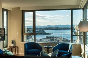 A room with a large window, two blue chairs, a small table, and a lamp. - New! Ocean and Mountain View King Suite (Victoria)