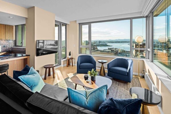 A modern living room with a sofa, chairs, a coffee table, and a TV. - New! Ocean and Mountain View King Suite (Victoria)