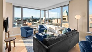 Ein modernes Wohnzimmer mit großem Fenster, einer schwarzen Couch, blauen Sesseln und einem kleinen Couchtisch.