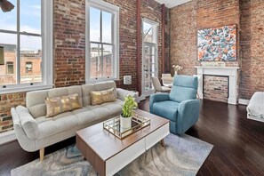 Ein Wohnzimmer mit Backsteinwand, einer Couch, einem blauen Sessel, einem Couchtisch und einem Kamin.