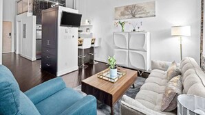 Een moderne woonkamer met een bank, een salontafel en een televisie. Er is een keukenhoek met kasten en een eettafel.