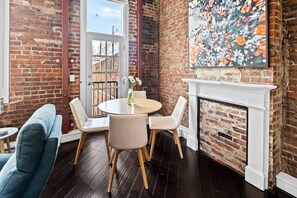 Ein Zimmer mit Backsteinwand, Kamin, rundem Esstisch mit Stühlen und einem blauen Sofa.