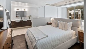 Een moderne slaapkamer met een groot bed, een kaptafel met spiegel en uitzicht op de stad door een groot raam.