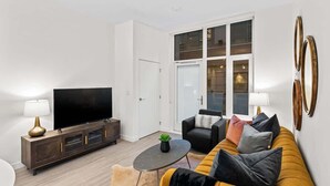 A modern living room with a sofa, TV, and a glass door leading to a balcony. - Affluent Executive Suite w/ Parking (Victoria)