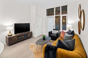 A modern living room with a sofa, TV, and a glass door leading to a balcony. - Affluent Executive Suite w/ Parking (Victoria)