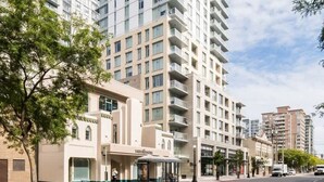 A multi-story hotel with a modern design, a central courtyard, and a street view with a bus stop. - Affluent Executive Suite w/ Parking (Victoria)