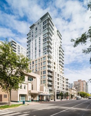 A multi-story hotel with a modern design, a central courtyard, and a street view with a bus stop. - Affluent Executive Suite w/ Parking (Victoria)