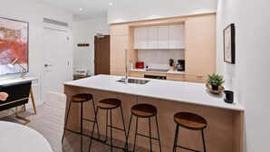 A modern kitchen with a central island, bar stools, and a dining area with a white table and chairs. - Affluent Executive Suite w/ Parking (Victoria)