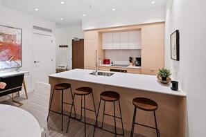 A modern kitchen with a central island, bar stools, and a dining area with a white table and chairs. - Affluent Executive Suite w/ Parking (Victoria)