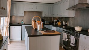 Una cocina con armarios azul claro, encimera negra, estufa y lavavajillas.