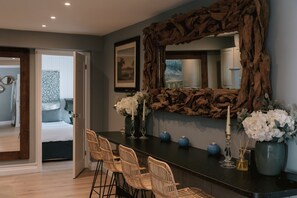 A modern room with a large mirror, wicker chairs, a dark countertop, and a bed with a blue and white patterned bedspread.