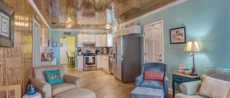 A spacious living area with a kitchen in the background, wooden ceiling, and light blue walls.