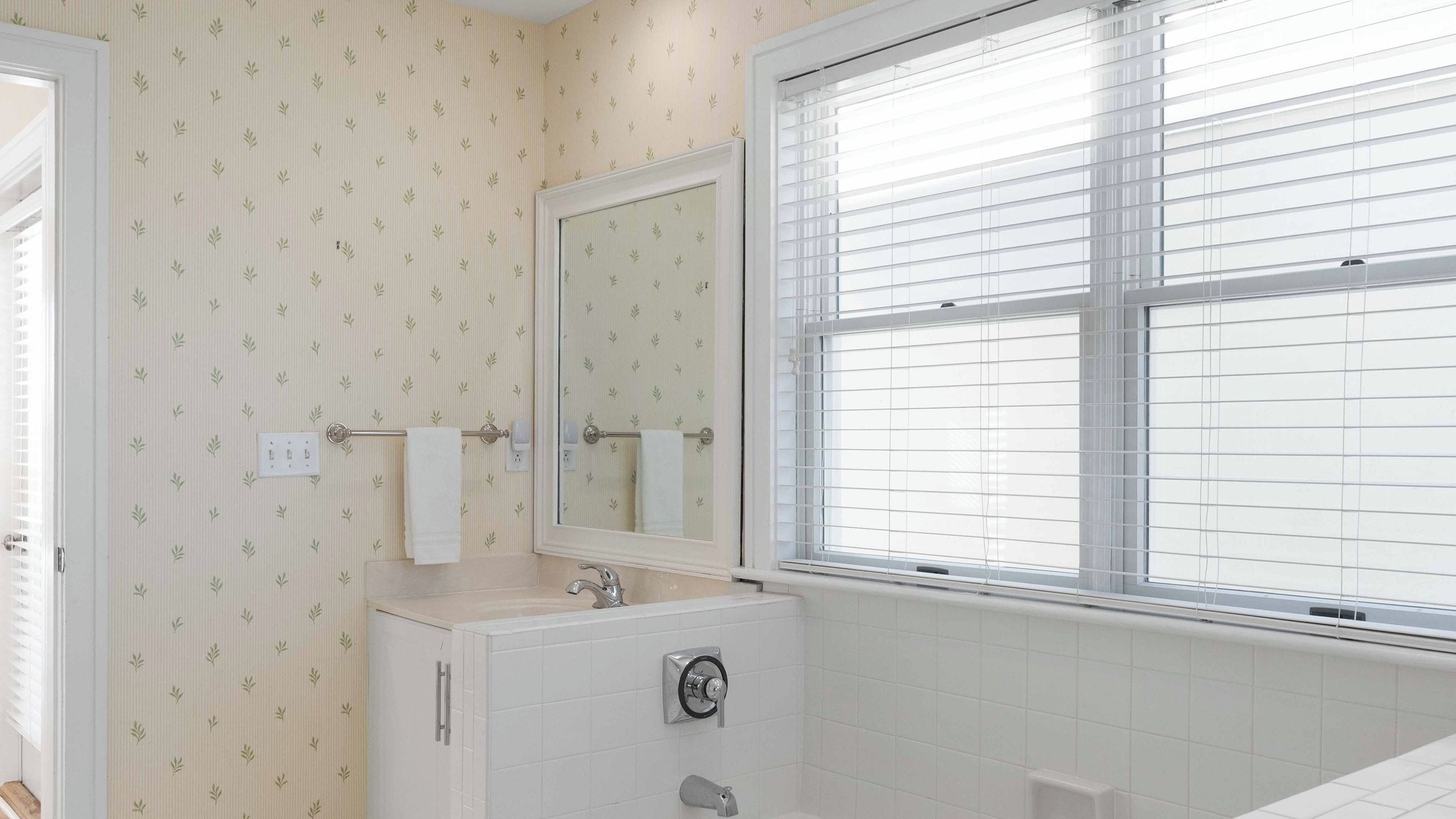 Une salle de bain avec une fenêtre, un miroir, un lavabo et un porte-serviettes.