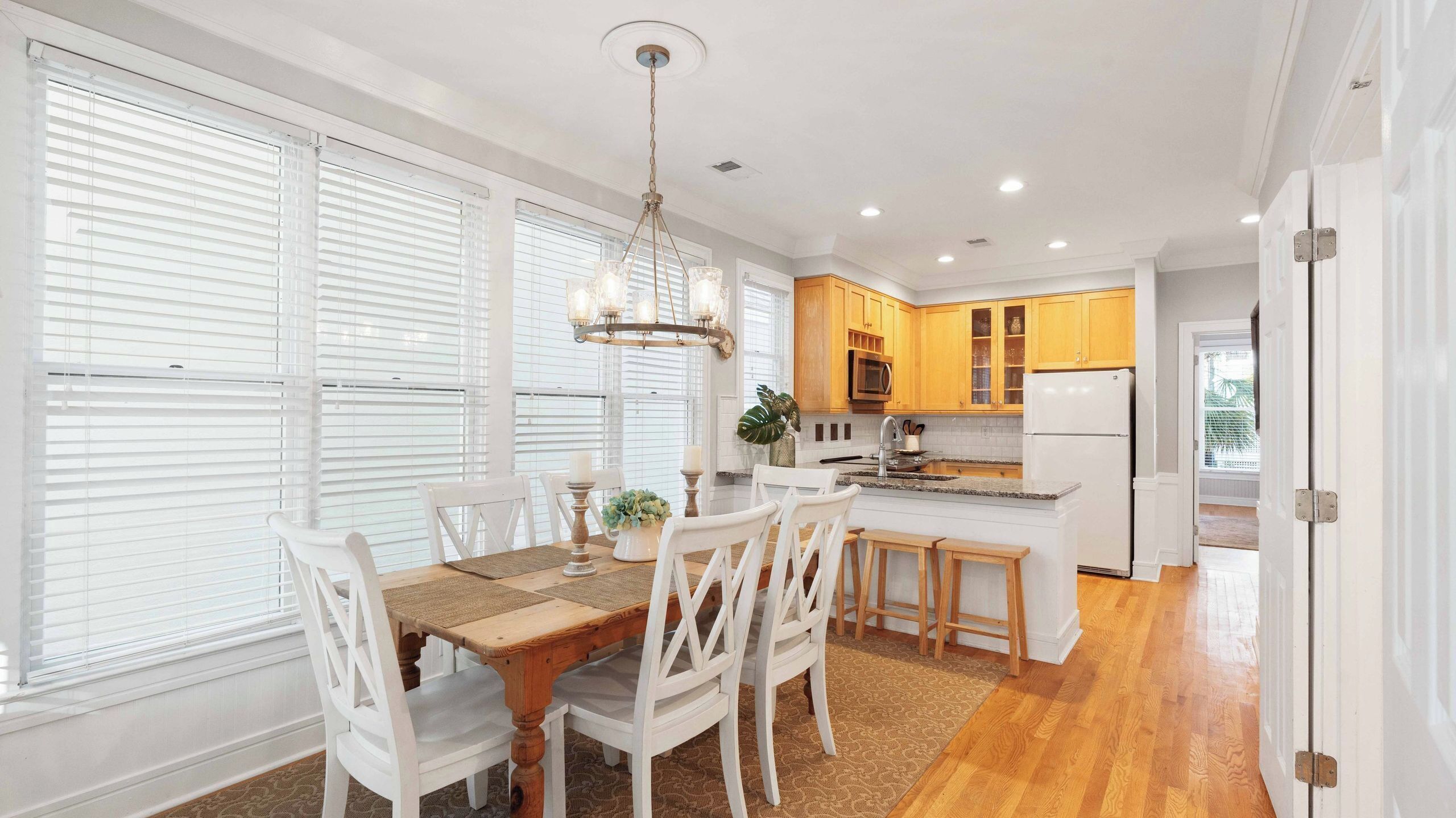 Una cocina moderna con armarios blancos, una isla central y un comedor con mesa de madera y sillas blancas.