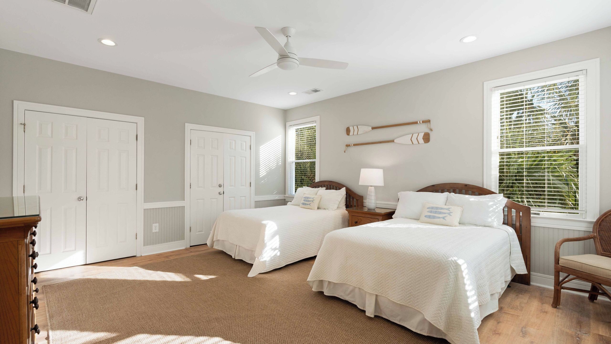 A bedroom with two beds, a ceiling fan, and large windows with blinds.