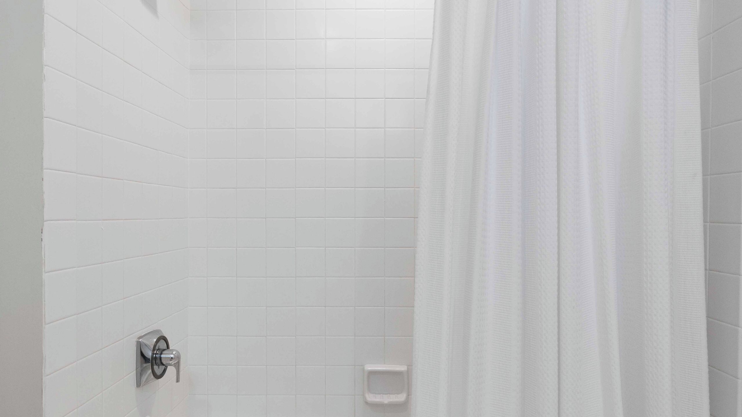 A bathroom with white tiled walls, a shower curtain, a toilet, and a faucet.