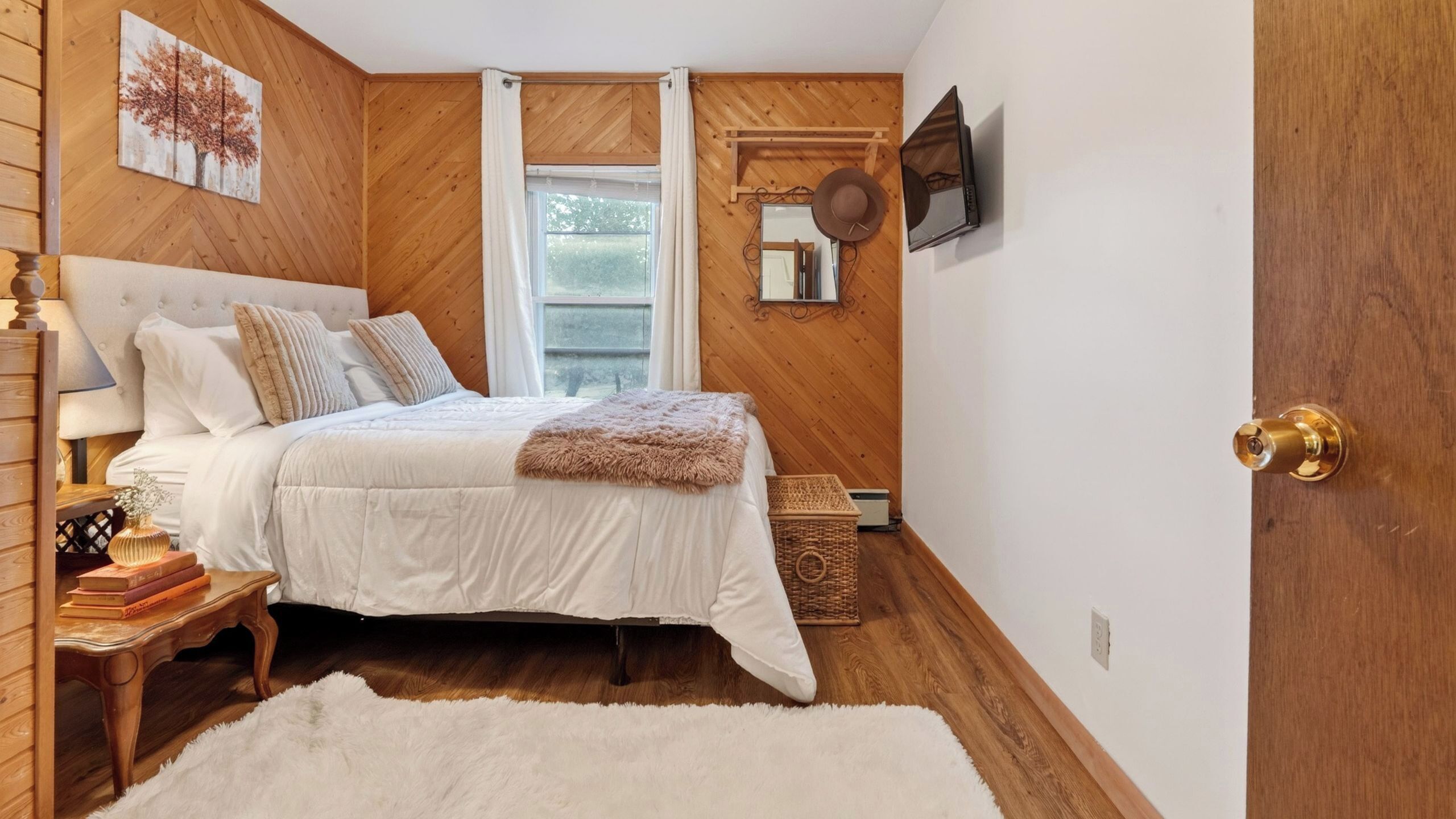A bedroom with a bed, a nightstand, a mirror, a window with curtains, and a door.