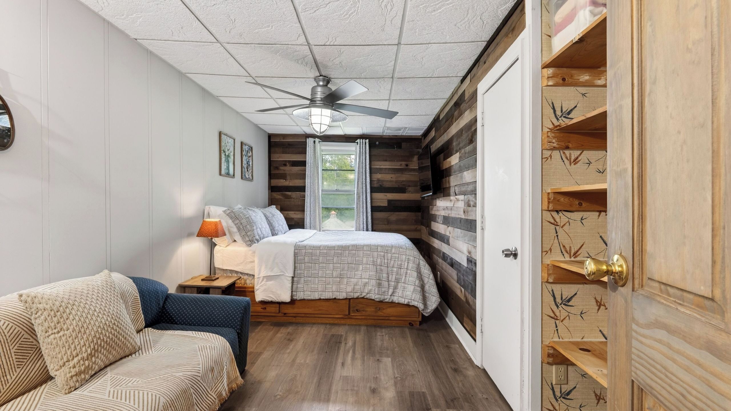 Ein Schlafzimmer mit Bett, Stuhl, Deckenventilator und einer Holztür mit Regalen.