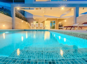 A modern indoor swimming pool with clear blue water, surrounded by lounge chairs and a sunbed, with a staircase leading to an upper level. - Villa Nexia with pool (Šibenik)