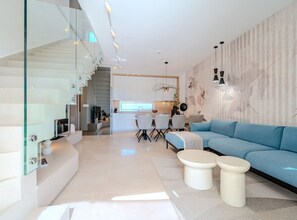 A modern interior with a staircase, a living area with a blue sofa, and a kitchen in the background. - Villa Nexia with pool (Šibenik)