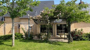 Een huis met een overdekt terras, een gazon en een boom.