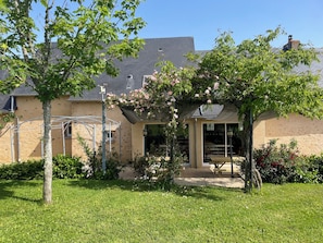 Ein Haus mit überdachter Terrasse, Rasen und Baum.