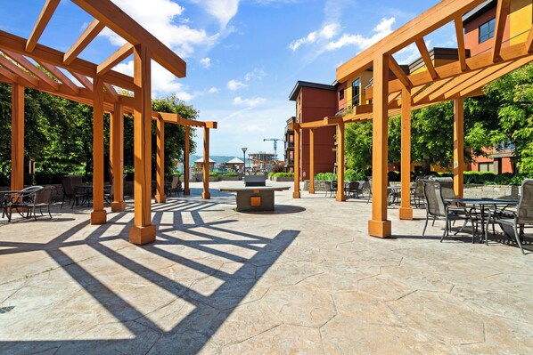 An outdoor patio area with wooden pergolas, stone flooring, and outdoor seating.