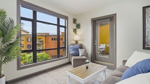 A modern living room with a large window, a sofa, a coffee table, and a door leading to a balcony.
